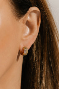 The model shows off the Sicily Hoop Pavé, its broad, golden hoop and cubic zirconia accents sparkling brightly on her ear. 