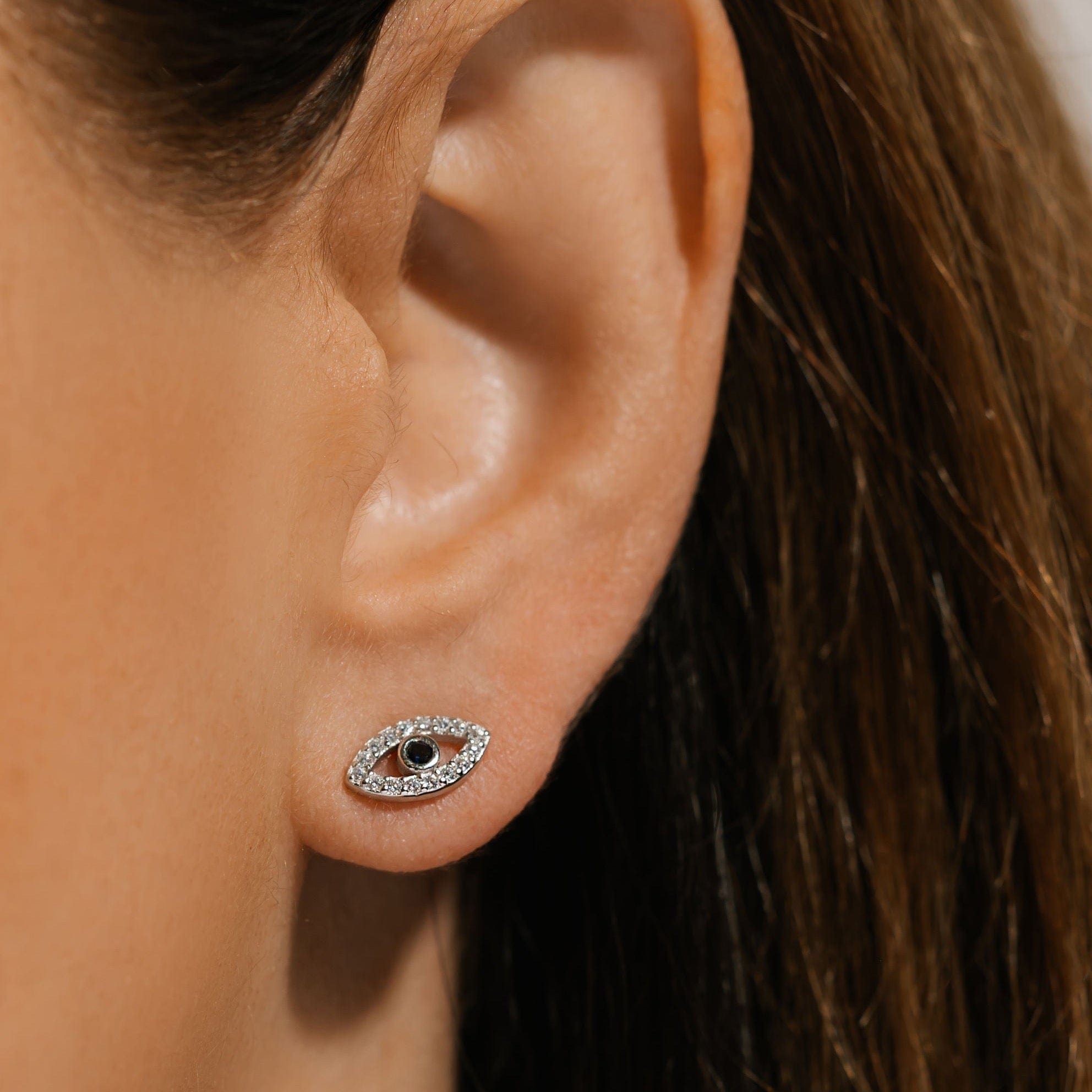 Sparkling crystal accents surround a stunning center sapphire as the sterling silver Evil Eye Cristallo Stud earring decorates the model's ear. 