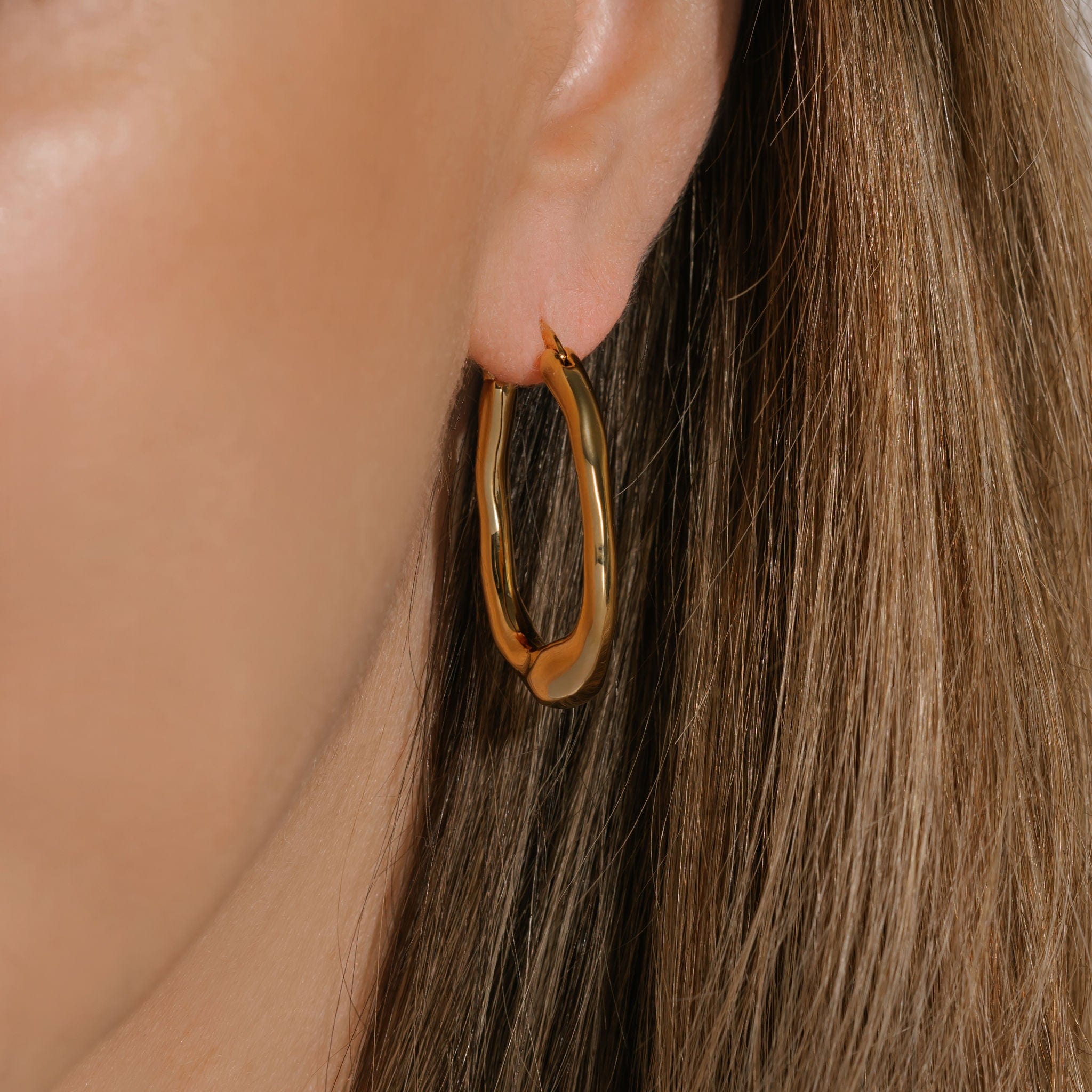 The Picasso Hoop is shown on the model's ear, the abstract shape of the hoop evident from the varying highlights and shadows along the golden surface. 