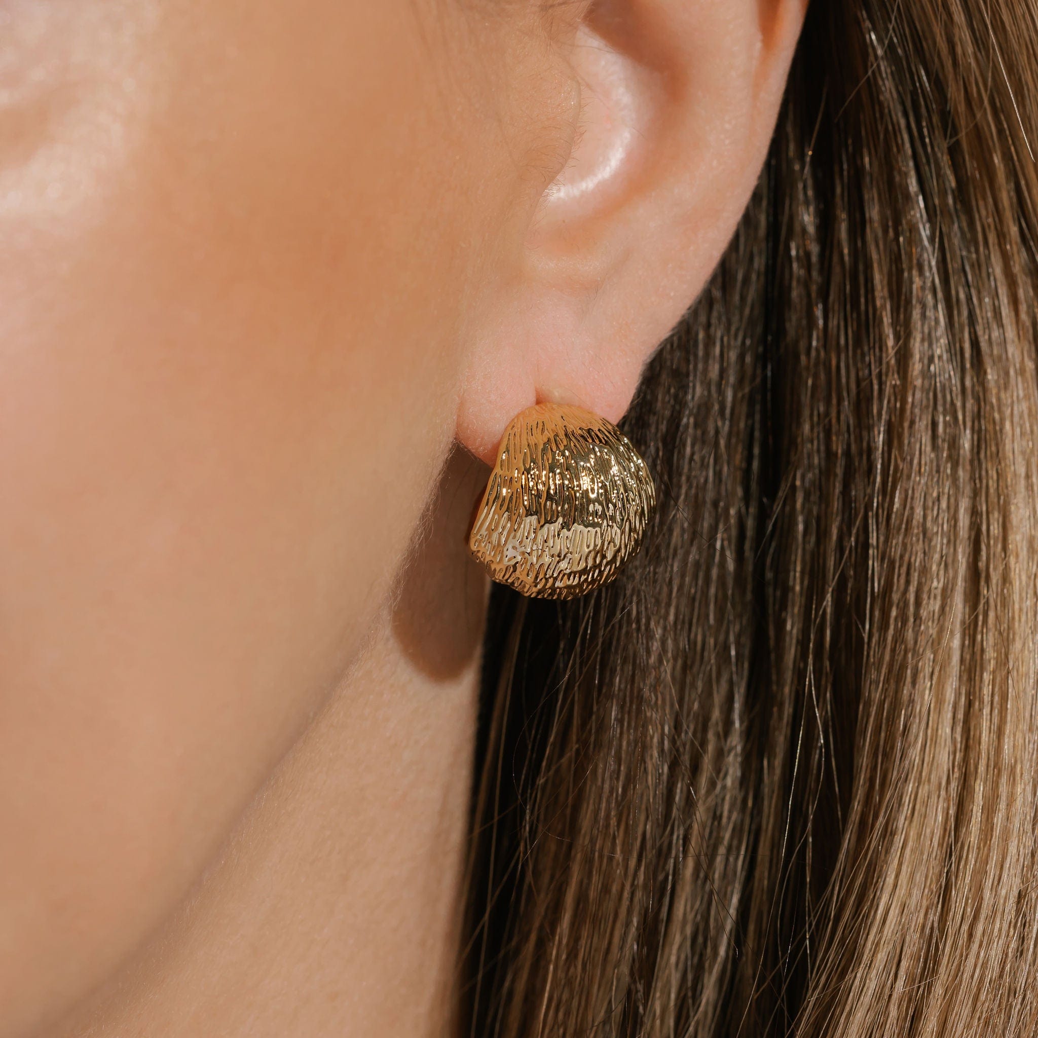 The golden, leaf-textured hoop of the Oro Hoop earring gracefully wraps around the model's ear lobe. 