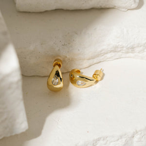 Two Amadora Hoop Mini earrings with crystal accents showcased on tiered stone slabs. 