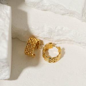 A pair Geneva Hoop earrings is displayed against white stone slabs, one standing upright to show off the chain link hoop while the second hoop lies on its side to display the full hoop shape and lever back closure. 