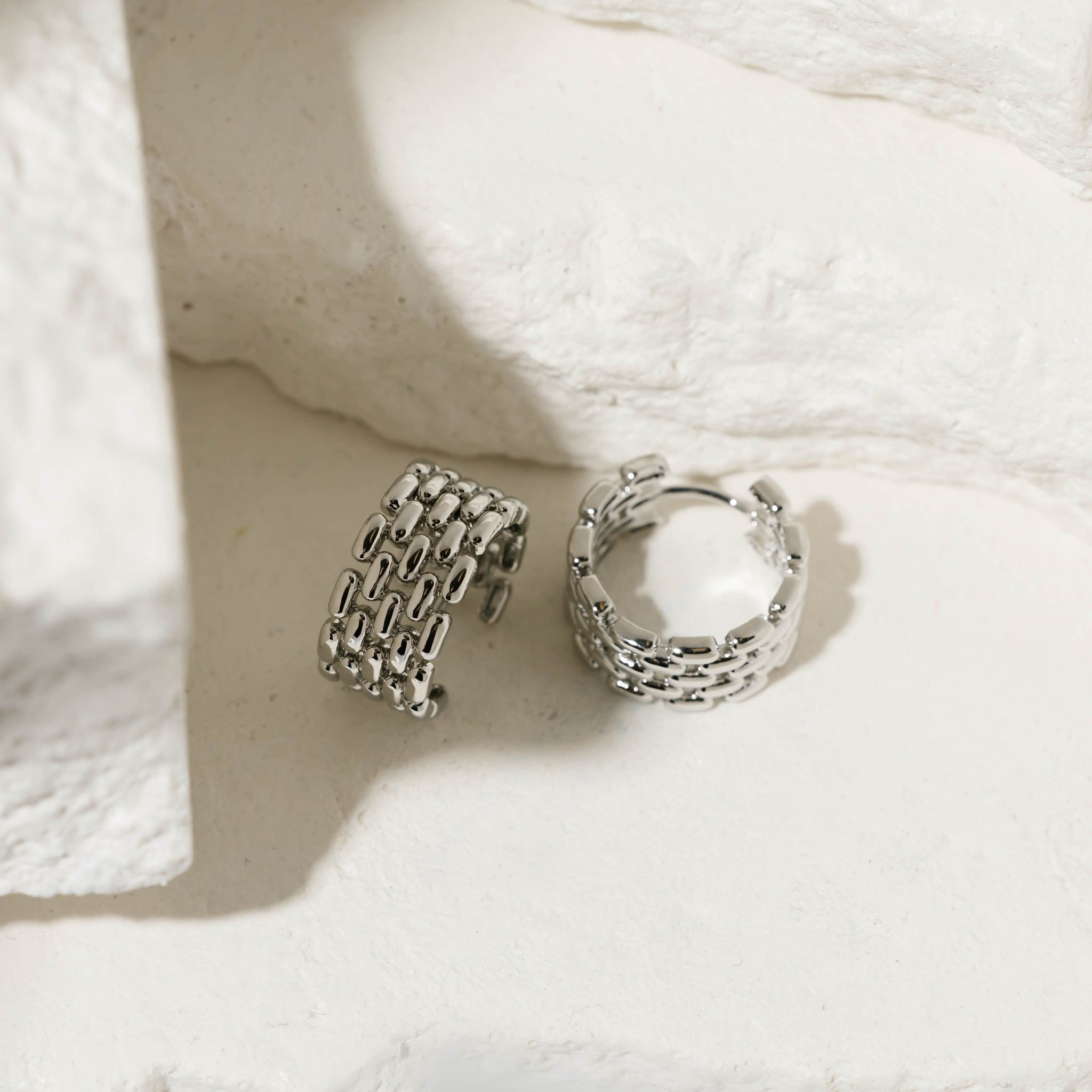 Two sterling silver Geneva Hoop earrings sit side by side on white stone slabs to showcase the chain link design and lever back closure. 