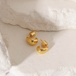 A pair of Amadora Huggie earrings lay together, showing off the golden curves and cylindrical pushback closures. 