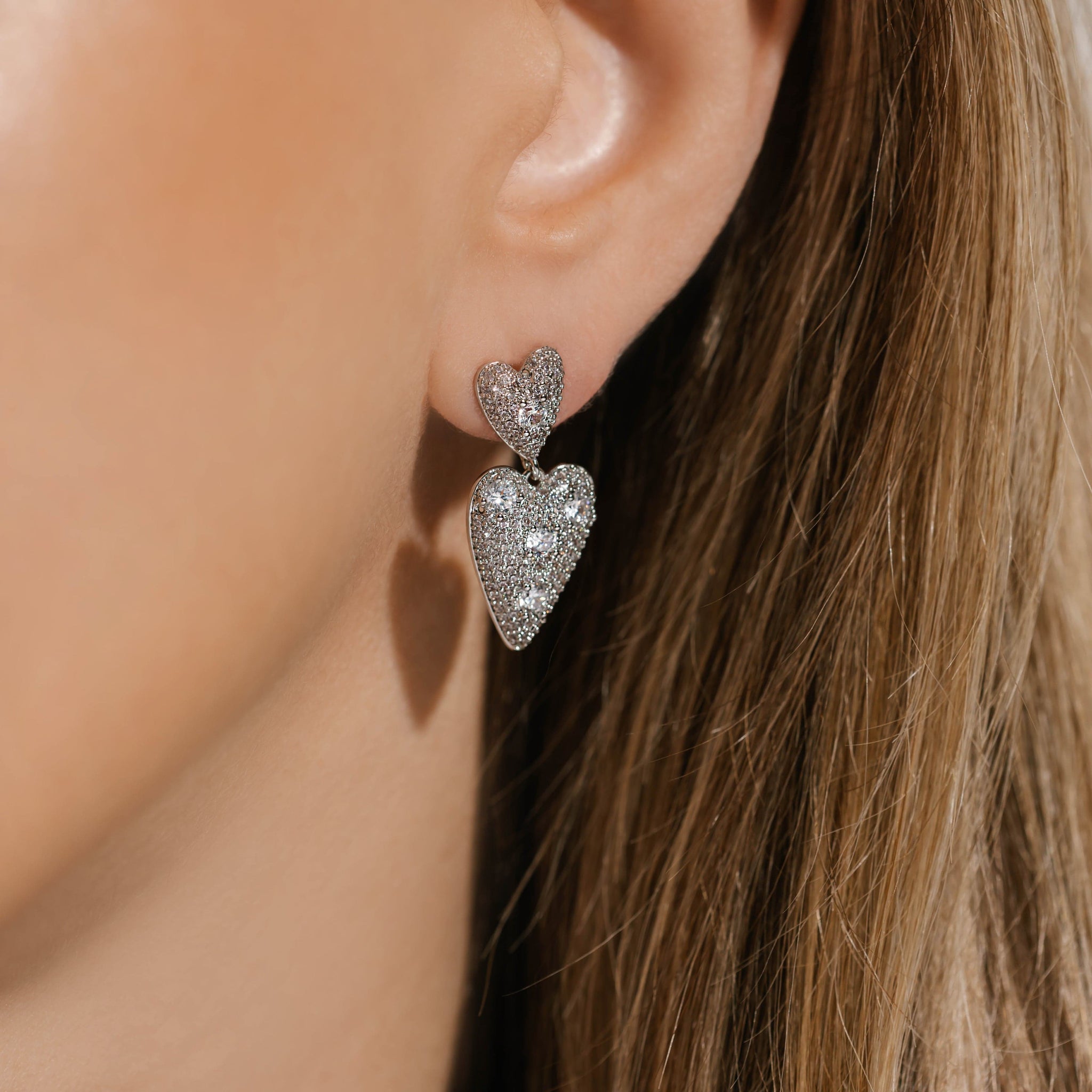 The two heart charms and pavé crystals that make up the Cupid Drop Hoop earrings sparkle brightly on the model's ear. 