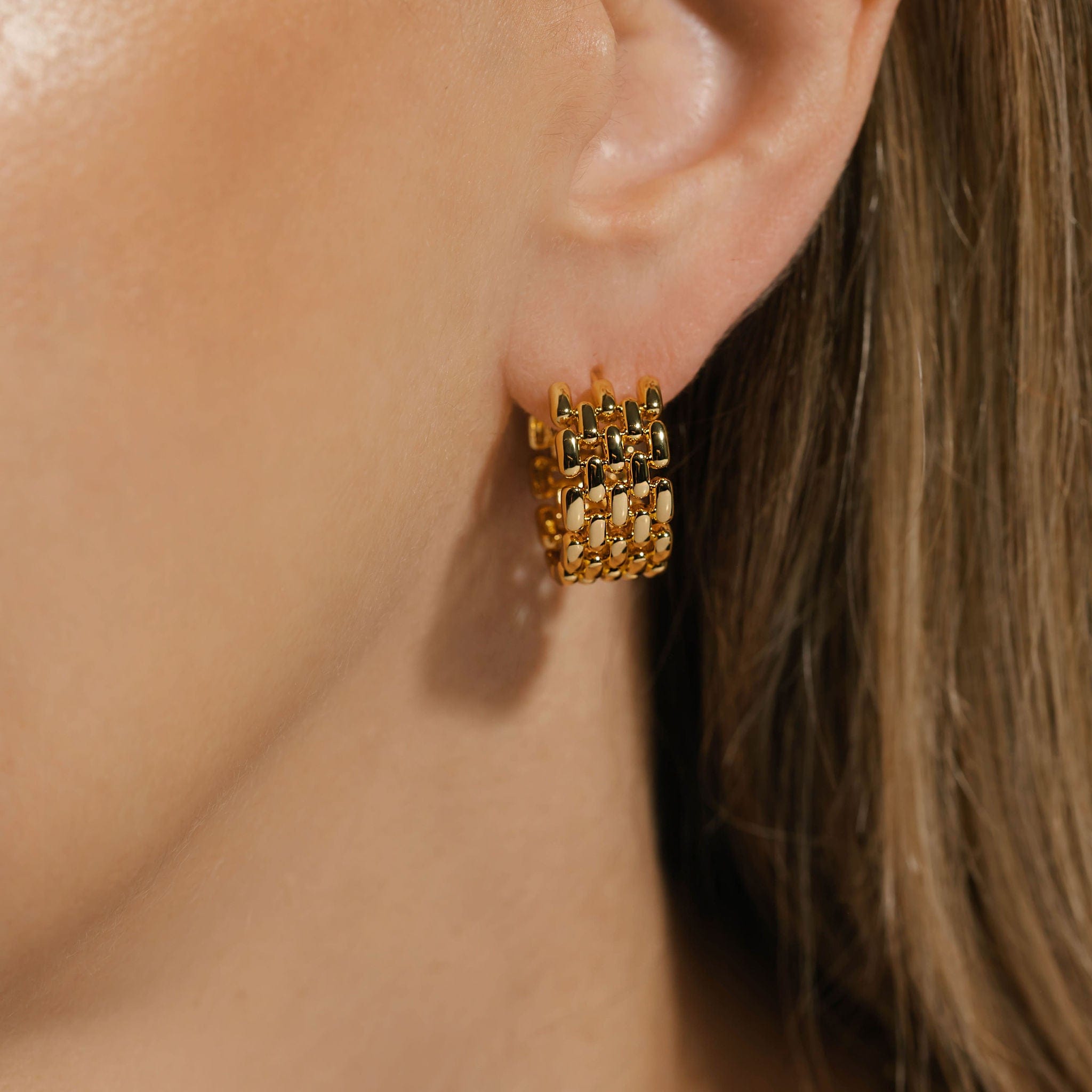 The golden chain links of the Geneva Hoop earring appear to cascade down from the earring adorning the model's ear.