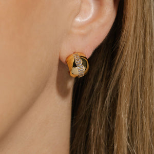 A golden Nice Hoop Scintilla earring adorns the model's ear as the sparkling crystal accents glimmer in the light. 