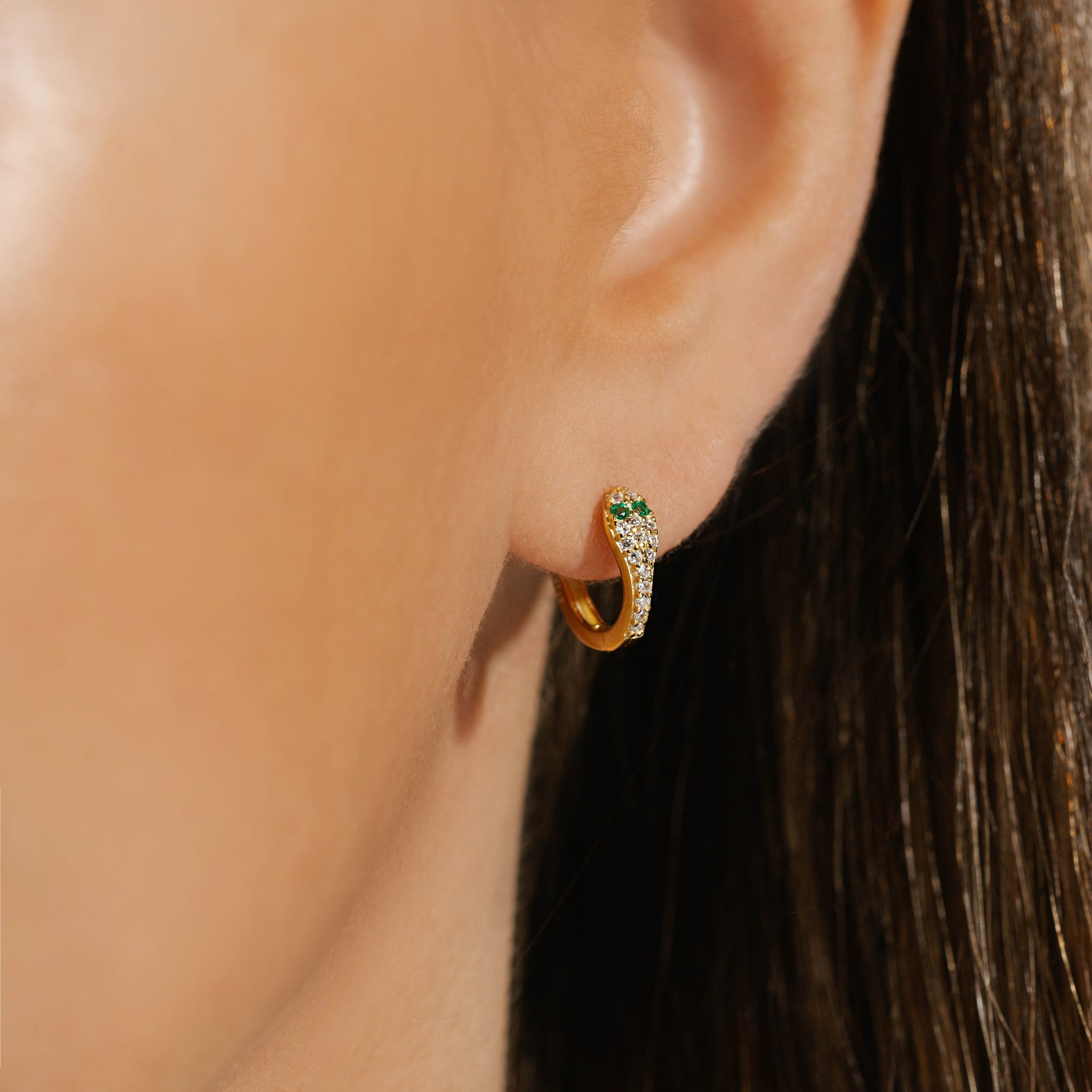 The Tentación Huggie earring wraps around the model's ear, the crystal-encrusted, snake-like front curve seeming to pierce her lobe with its elegant design. 