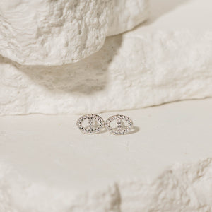 The Jolie Stud pavé earrings in sterling silver, featuring a delicate circular design encrusted with sparkling crystals, displayed on a natural stone background. Sterling silver pavé stud earrings by The Perfect Hoop.