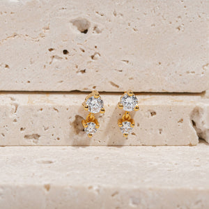 The posts of a pair of Luxe Drop Stud earrings are supported between stone slabs, allowing the smaller pendants to fall along the side of the lower stone.