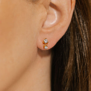 The Luxe Drop Stud earring glistens on the model's ear, the larger crystal hugging her earlobe as the smaller crystal hangs gracefully beneath it. 