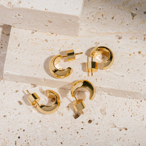 The two pairs of earrings in the Nice Huggie Duo lay together on tiered stone slabs to display the smooth open hoops and cylindrical pushback closures. 