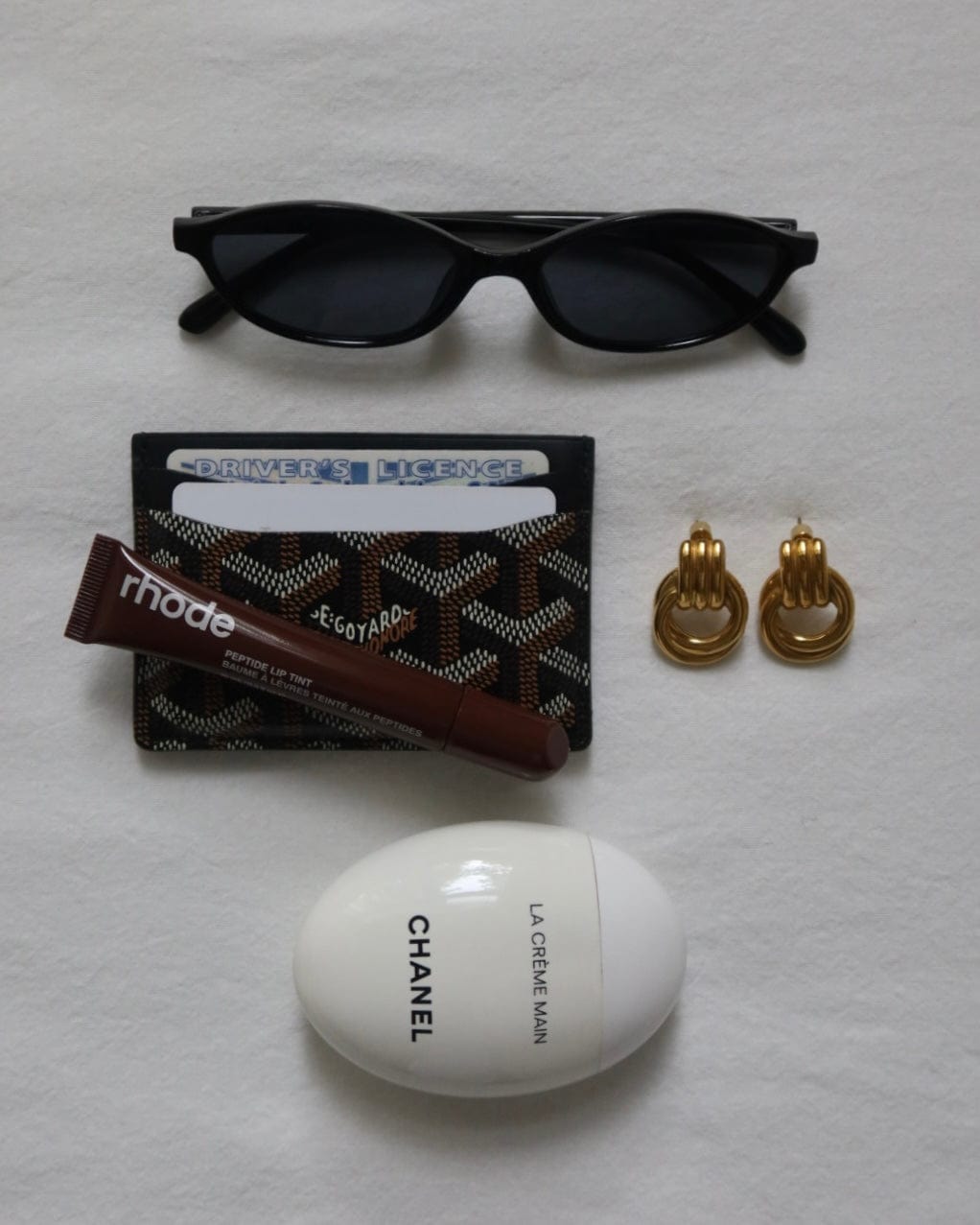 Flat lay featuring The Perfect Hoop Lupo Hoops in gold, styled with designer sunglasses, lip balm, chocolate bar, and travel essentials