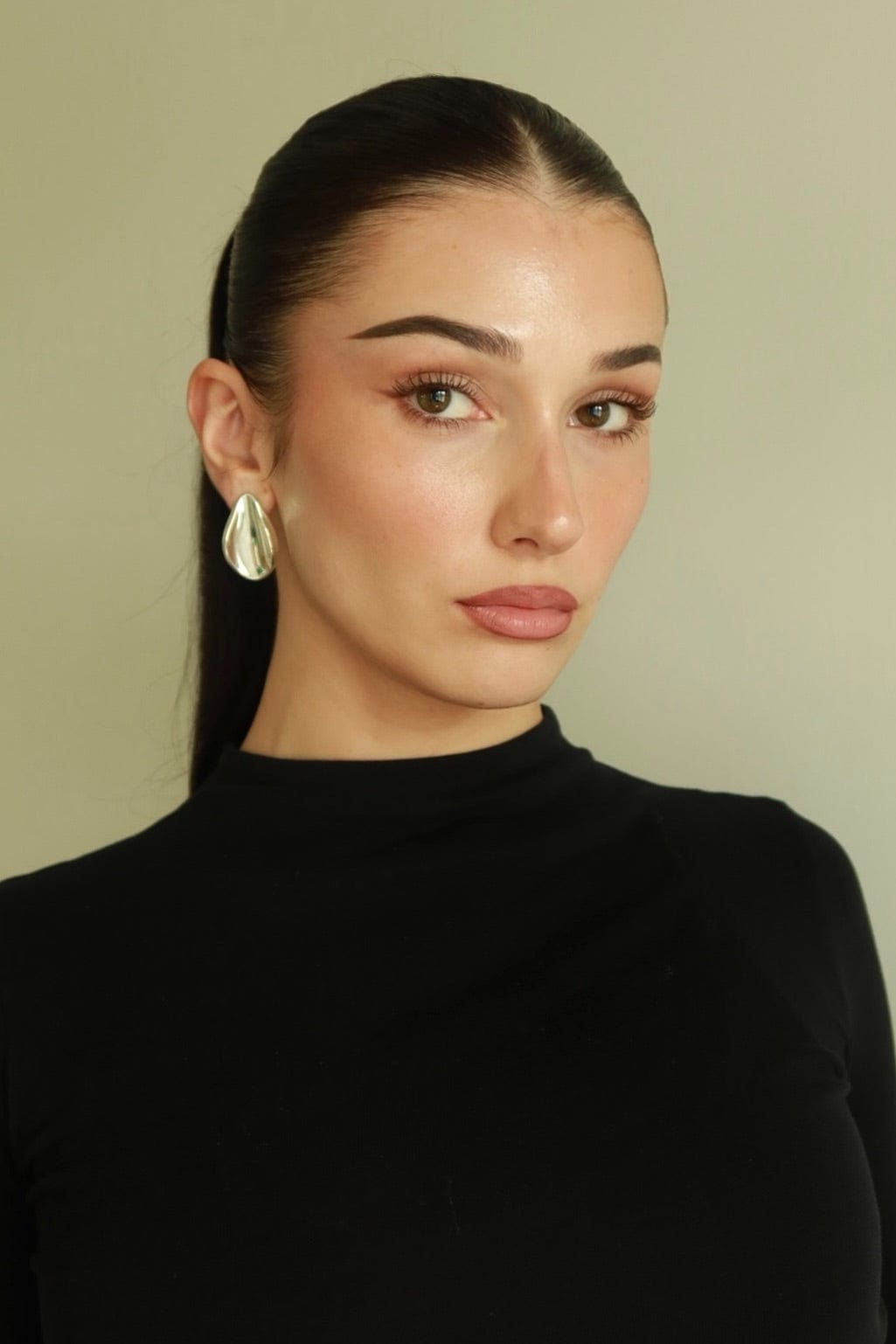Model wearing The Perfect Hoop’s Harlow Earring in silver, a sculptural drop hoop with a modern twisted silhouette, styled with a sleek ponytail and black high-neck top.