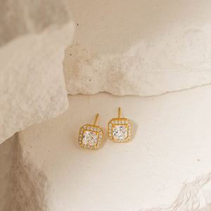 A pair of Principessa Stud earrings lay side by side on tiered stone slabs to showcase the princess cut crystals and surrounding crystal accents. 