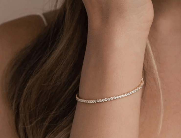 Close-up of a person's wrist wearing a delicate diamond tennis bracelet with a neutral background.