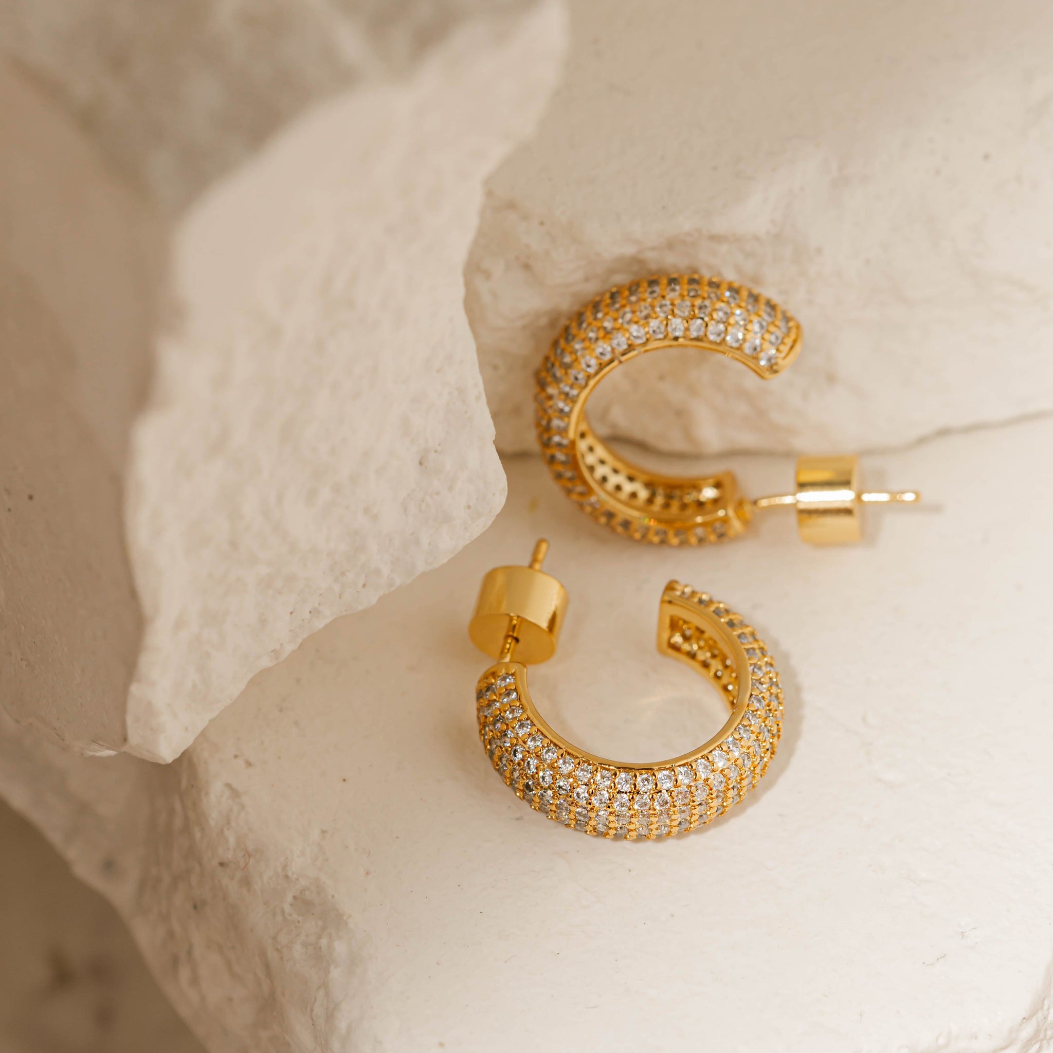 Two Siena Hoop Pavé earrings are displayed, one laying on its side as the other balances on its upper curve and cylindrical closure. 