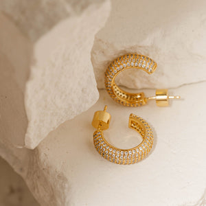 Two Siena Hoop Pavé earrings are displayed, one laying on its side as the other balances on its upper curve and cylindrical closure. 