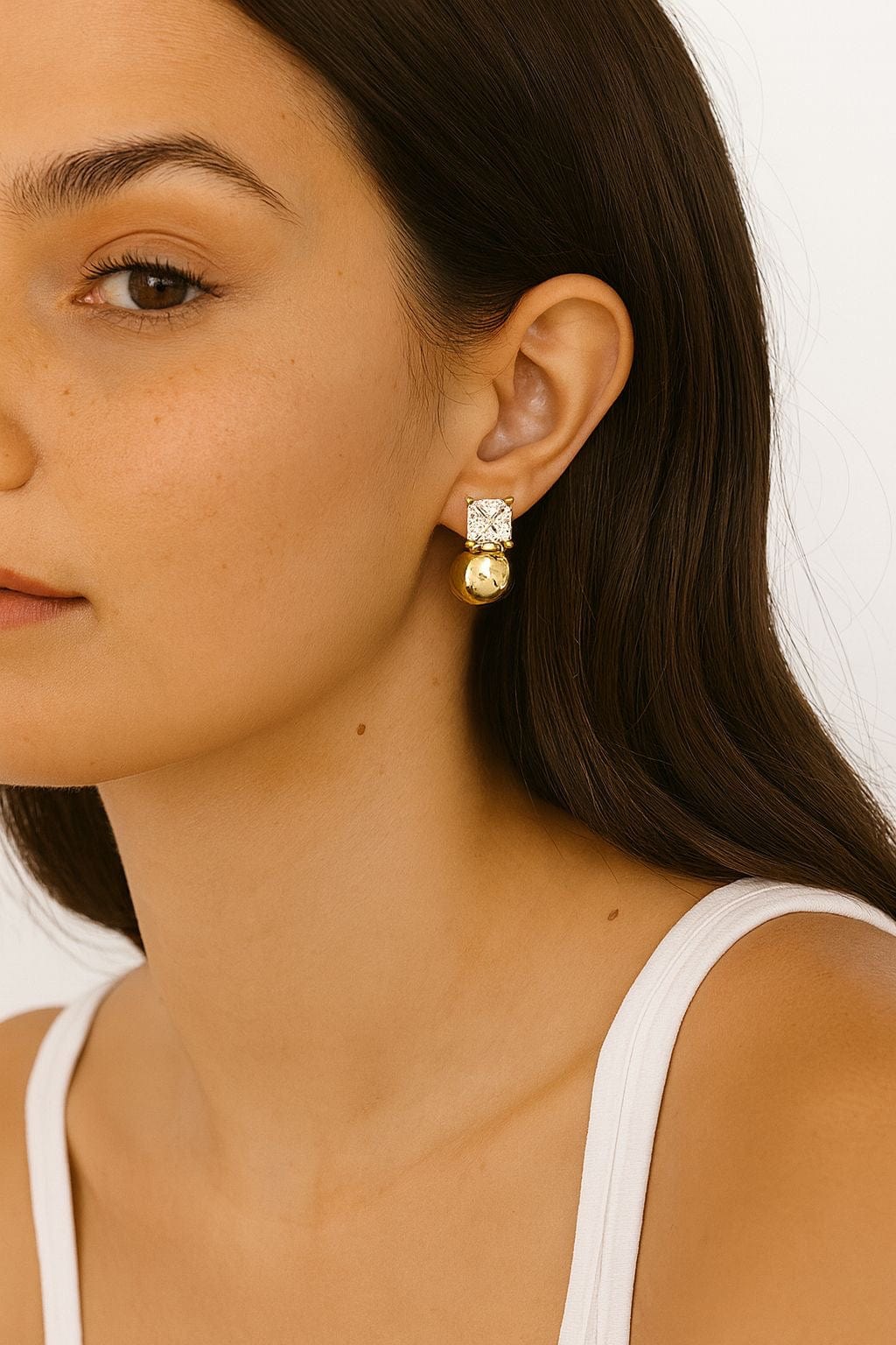 The Perfect Hoop Sofi Stud Earrings worn by model with long dark hair, showcasing the clear crystal and gold ball drop combination, styled with a white tank top on neutral background