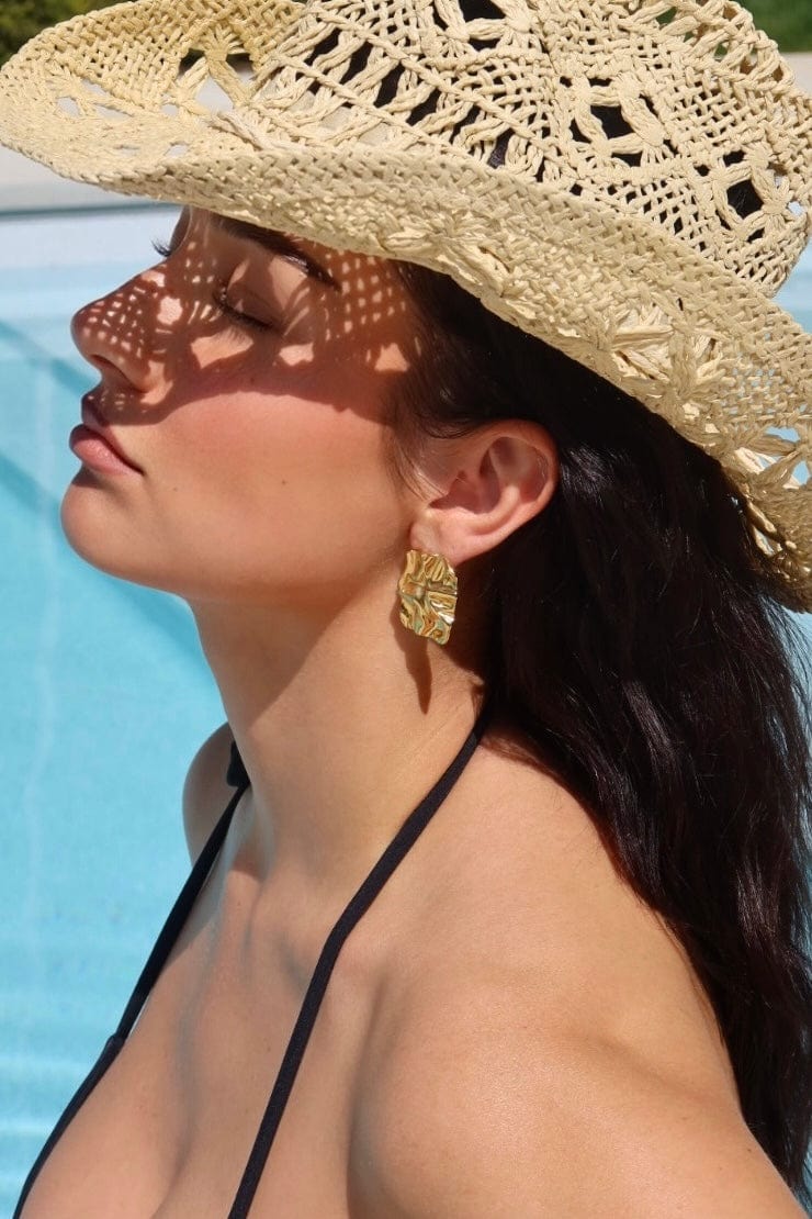 Model wearing a straw hat and gold earrings  by The Perfect Hoop, by a poolside