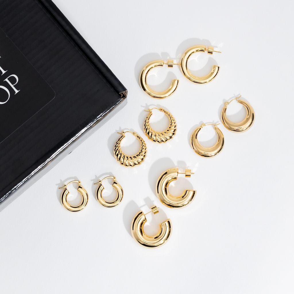  The five golden pairs of classically styled hoop earrings in The Icons Hoop Starter Pack are neatly arranged along the edge of a black gift box.
