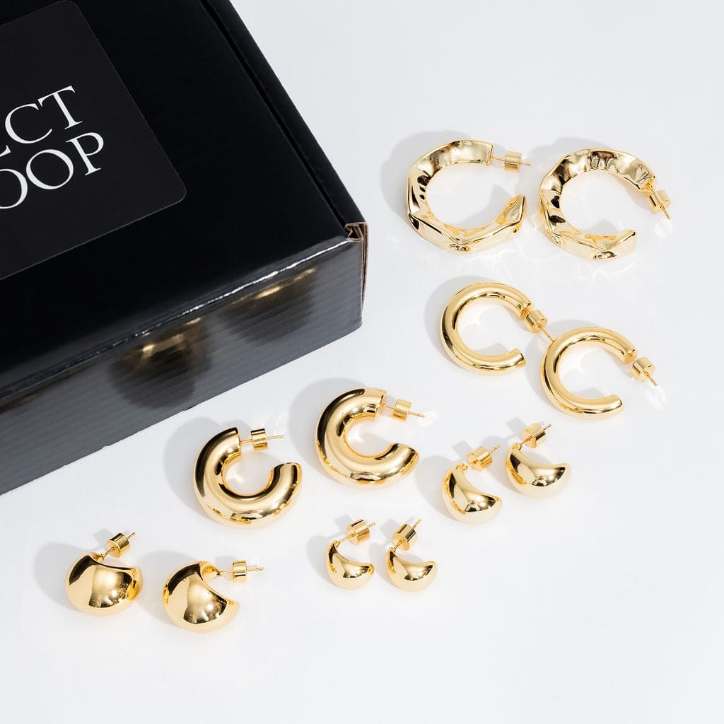 The large and chunky open hoop earrings included in the Make a Statement Hoop Starter Pack are displayed on a white counter next to the black box they come packaged in. 
