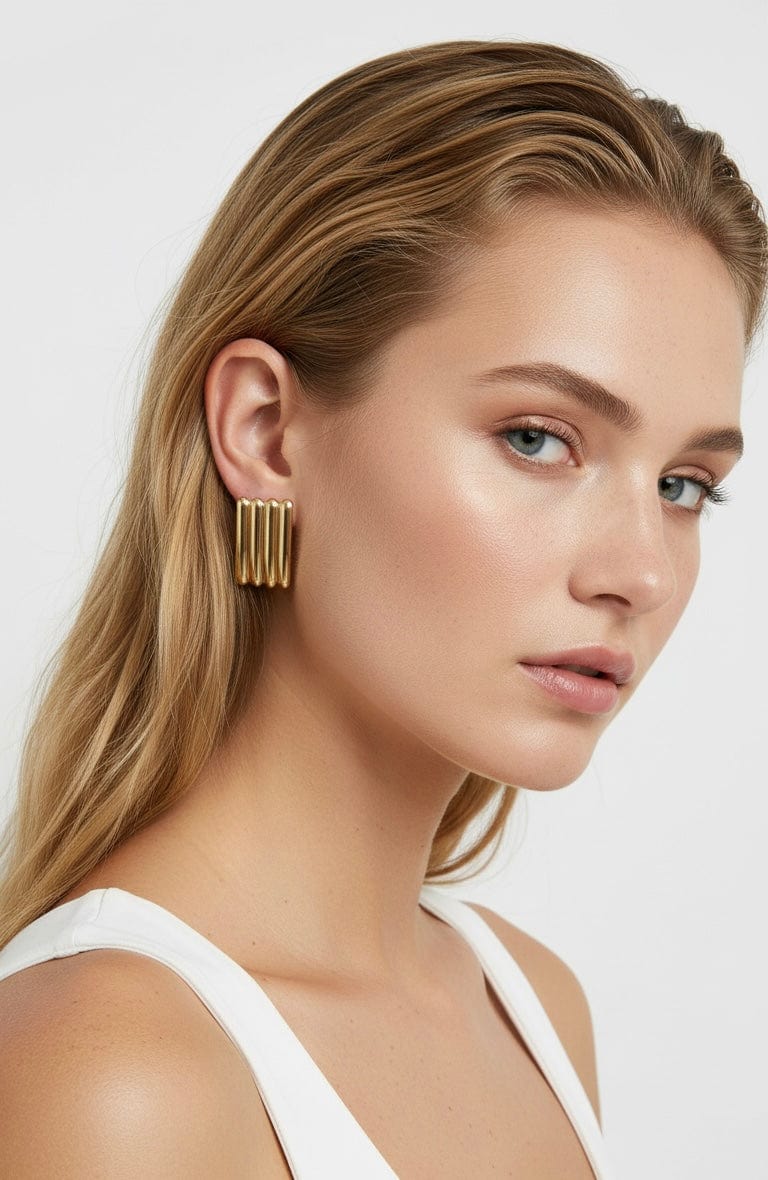 Model wearing The Perfect Hoop Terra Earrings in polished gold, featuring stacked ridged bars for a bold sculptural look, paired with sleek side-parted hair and white tank.