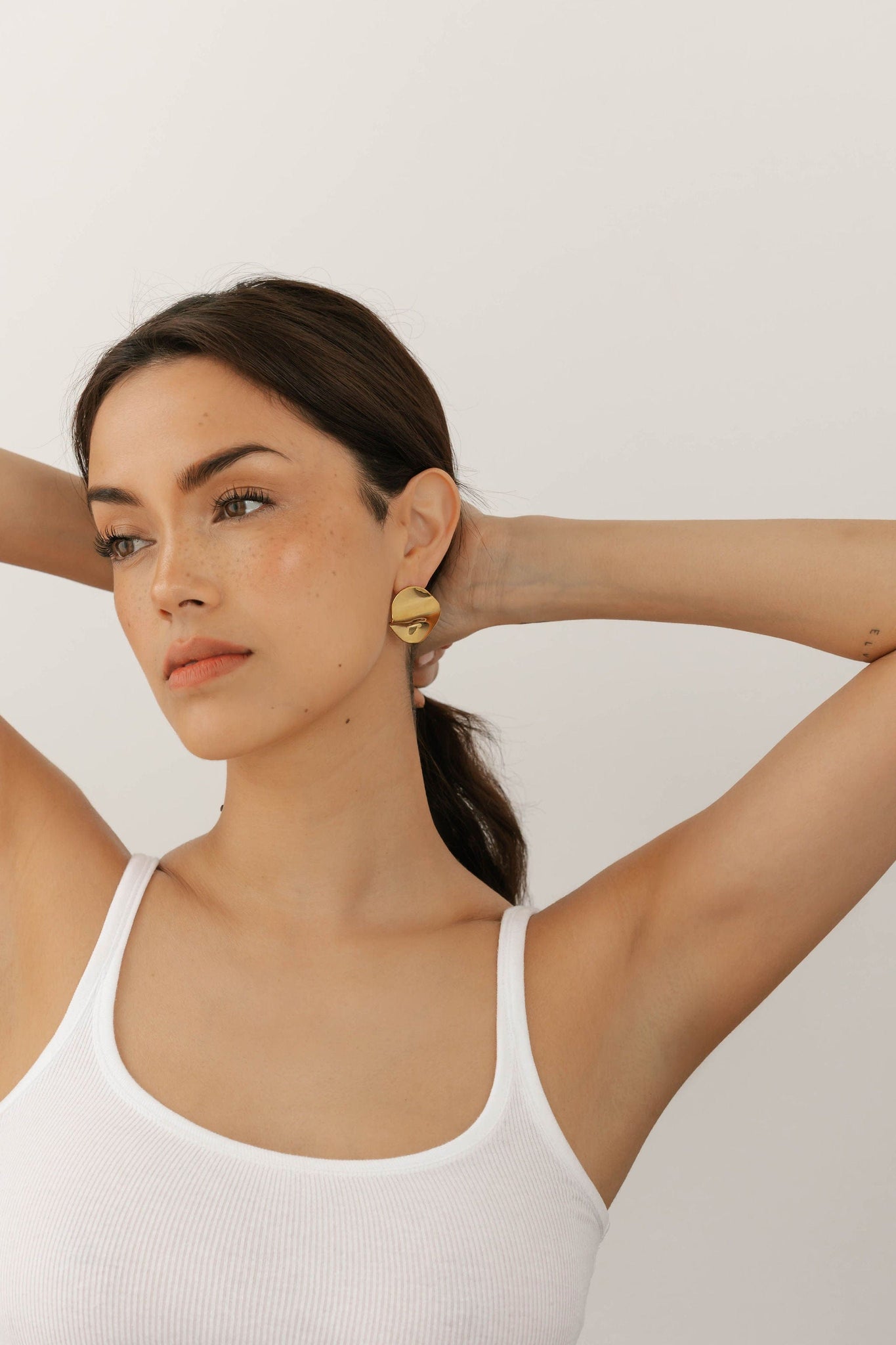 The Perfect Hoop Aurora Earring, model wearing asymmetric drop earrings with hand-molded gold detailing and faceted crystals for a statement look.