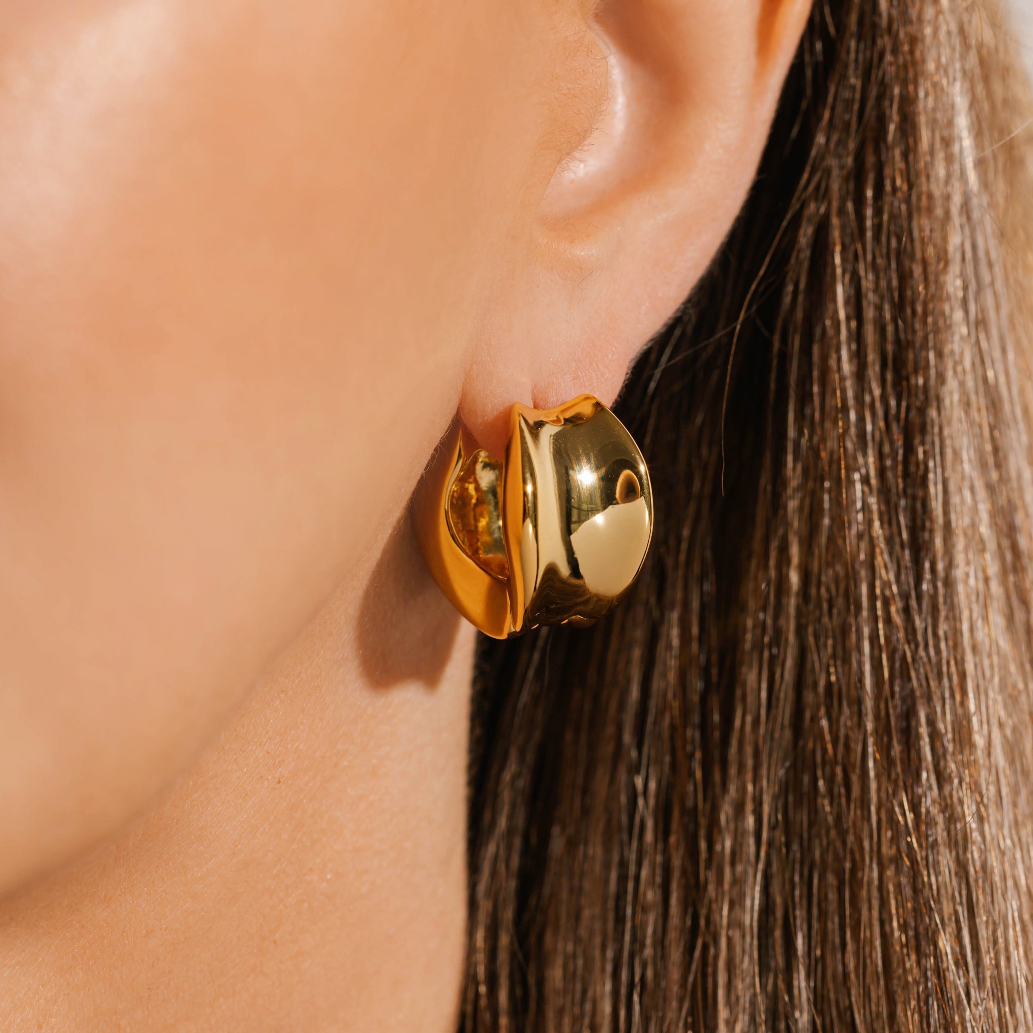 The bold, indented face of the Chateaux Hoop reflects its surroundings as it adorns the model's ear. 