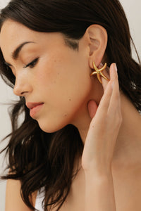 Model wearing the Estelle gold starfish earring, touching her ear gently to highlight the sculptural design.  By The Perfect Hoop.