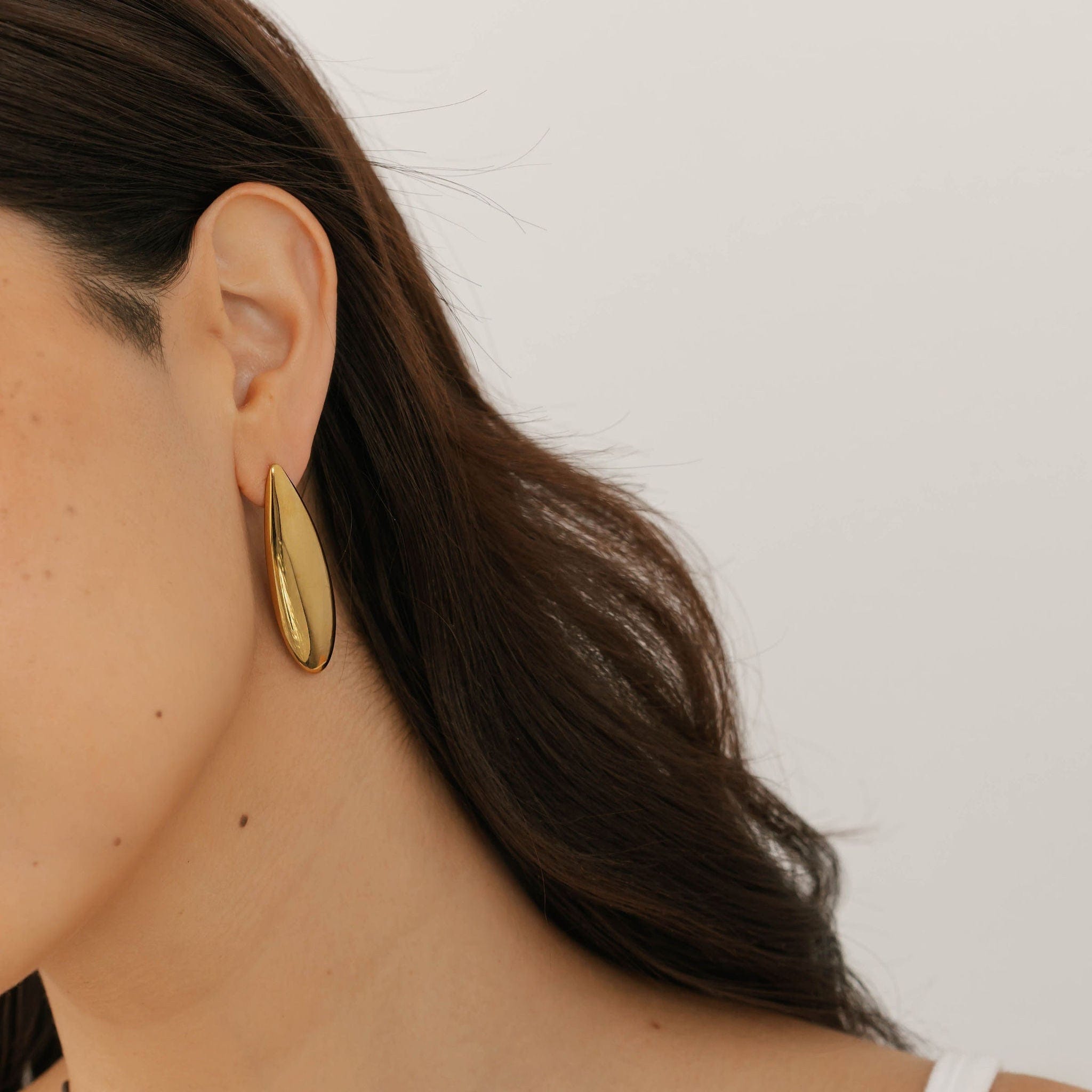 Model wearing The Perfect Hoop Lotus Earring, a sculptural gold drop earring with an elongated teardrop shape and mirror-like shine.