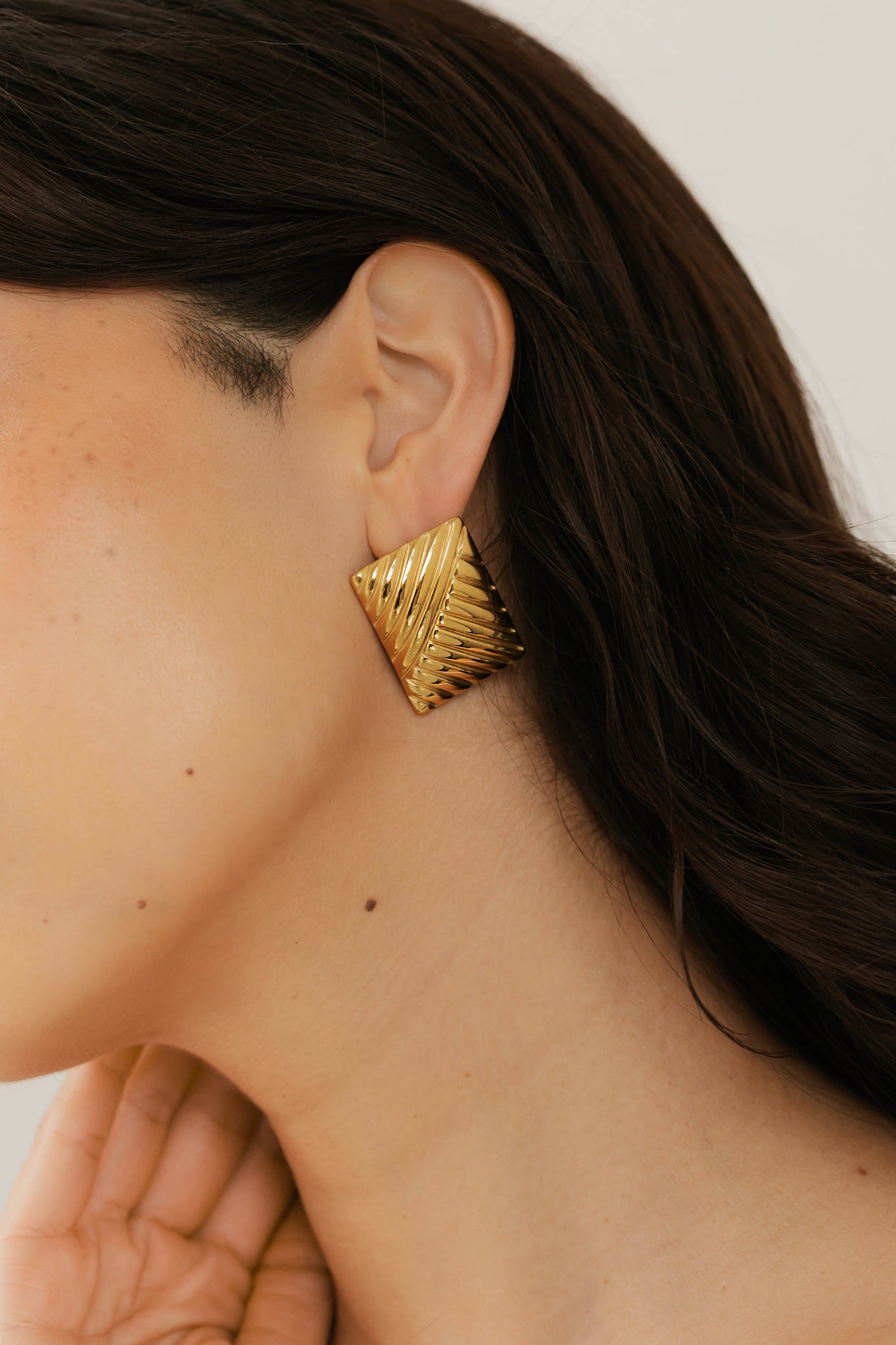 Close-up of The Selene Earring by The Perfect Hoop worn on the ear, highlighting the luxe gold finish and ribbed pattern against natural skin tone and dark hair.
