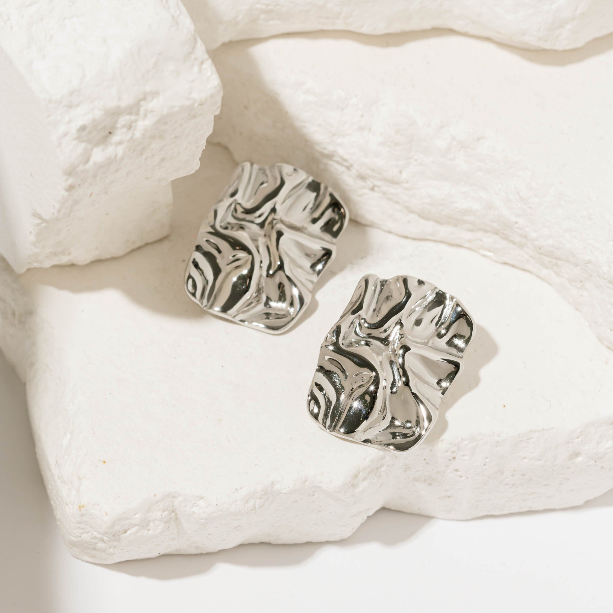 The Perfect Hoop Soleil Hoop in polished silver, sculptural textured earrings displayed flat on white stone backdrop with soft shadows.