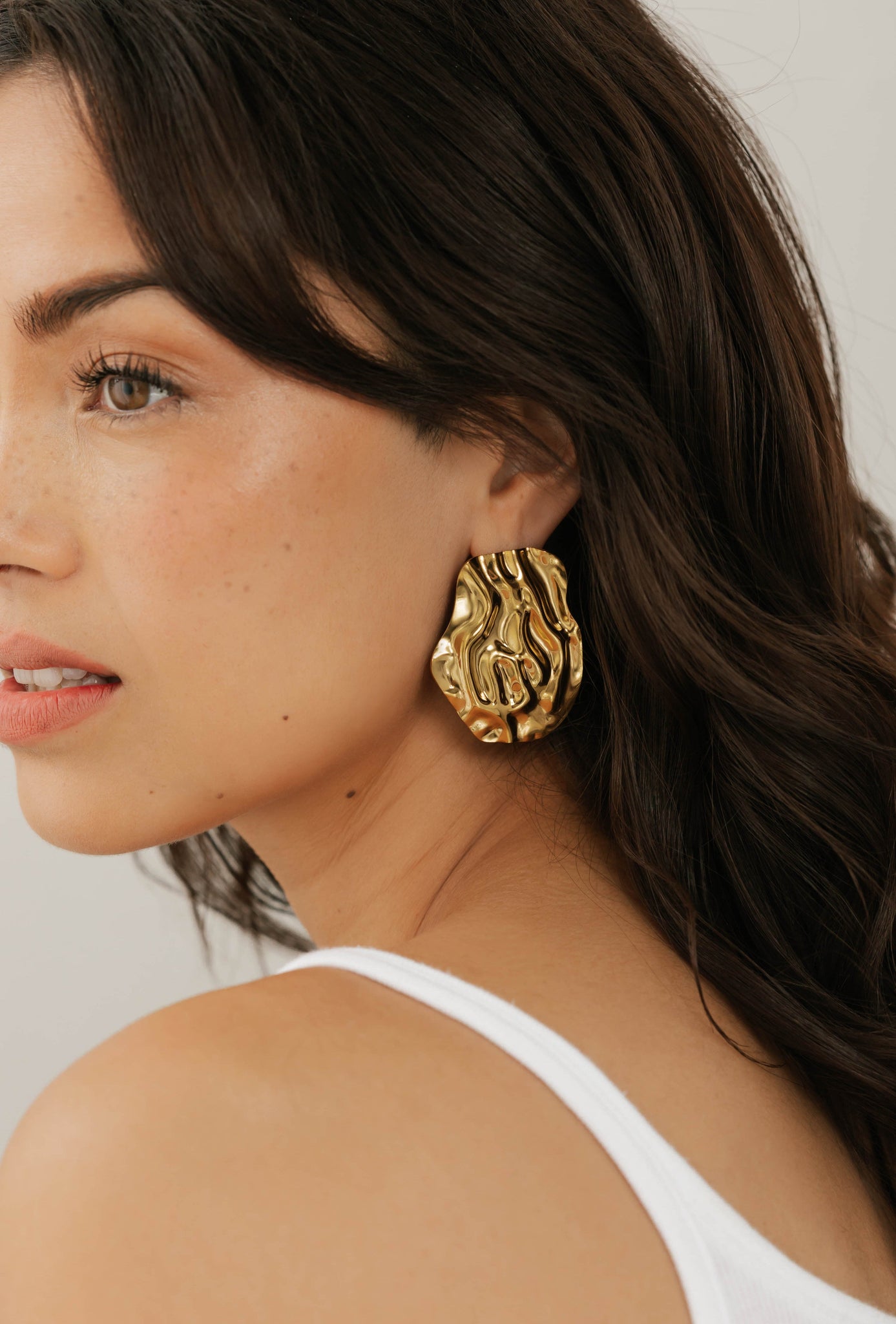 Side profile of model wearing The Spritz Earring by The Perfect Hoop, featuring a bold gold abstract shape with a high-shine finish, against a neutral background.
