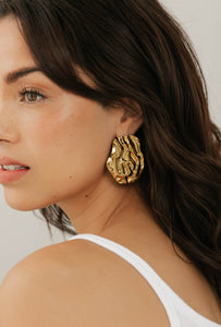 Side profile of model wearing The Spritz Earring by The Perfect Hoop, featuring a bold gold abstract shape with a high-shine finish, against a neutral background.