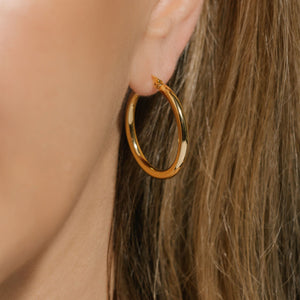The golden Allegra Hoop is a beautiful, medium sized hoop glimmering accent on the model's ear. ByThe Perfect Hoop