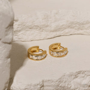 Gold-plated Almeria Hoop earrings adorned with brilliant cubic zirconia stones, elegantly showcased on a textured stone surface, highlighting their luxurious and timeless appeal.