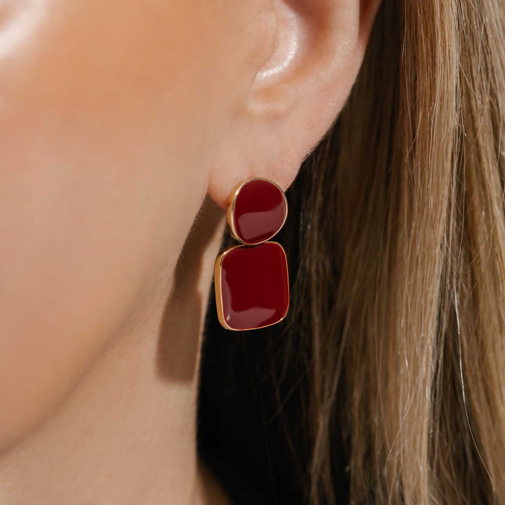 Model wearing The Merlot Hoop earrings featuring bold, geometric red enamel accents framed in gold, offering a striking and sophisticated statement look.