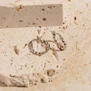 A pair of Corda Huggie Platinum earrings is displayed on a counter, one hoop laying on its side and the other propped up to show the twisted design from every angle. 