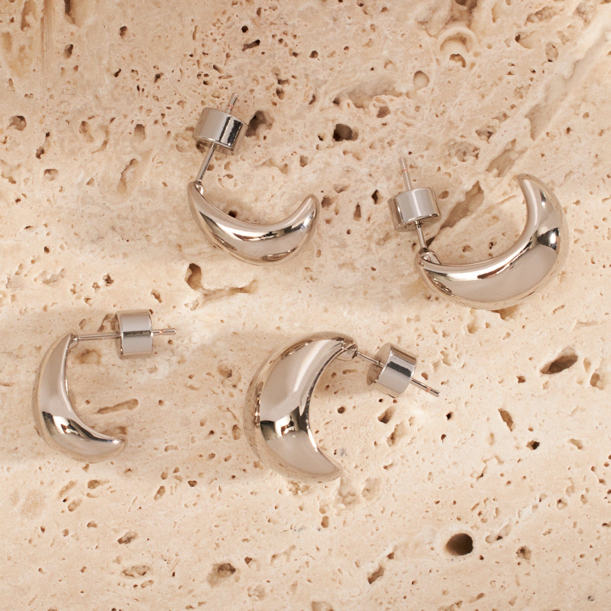 The four earrings in the Amadora Hoop Duo Platinum set lay on a stone counter to display their crescent shape and sleek silver finish.