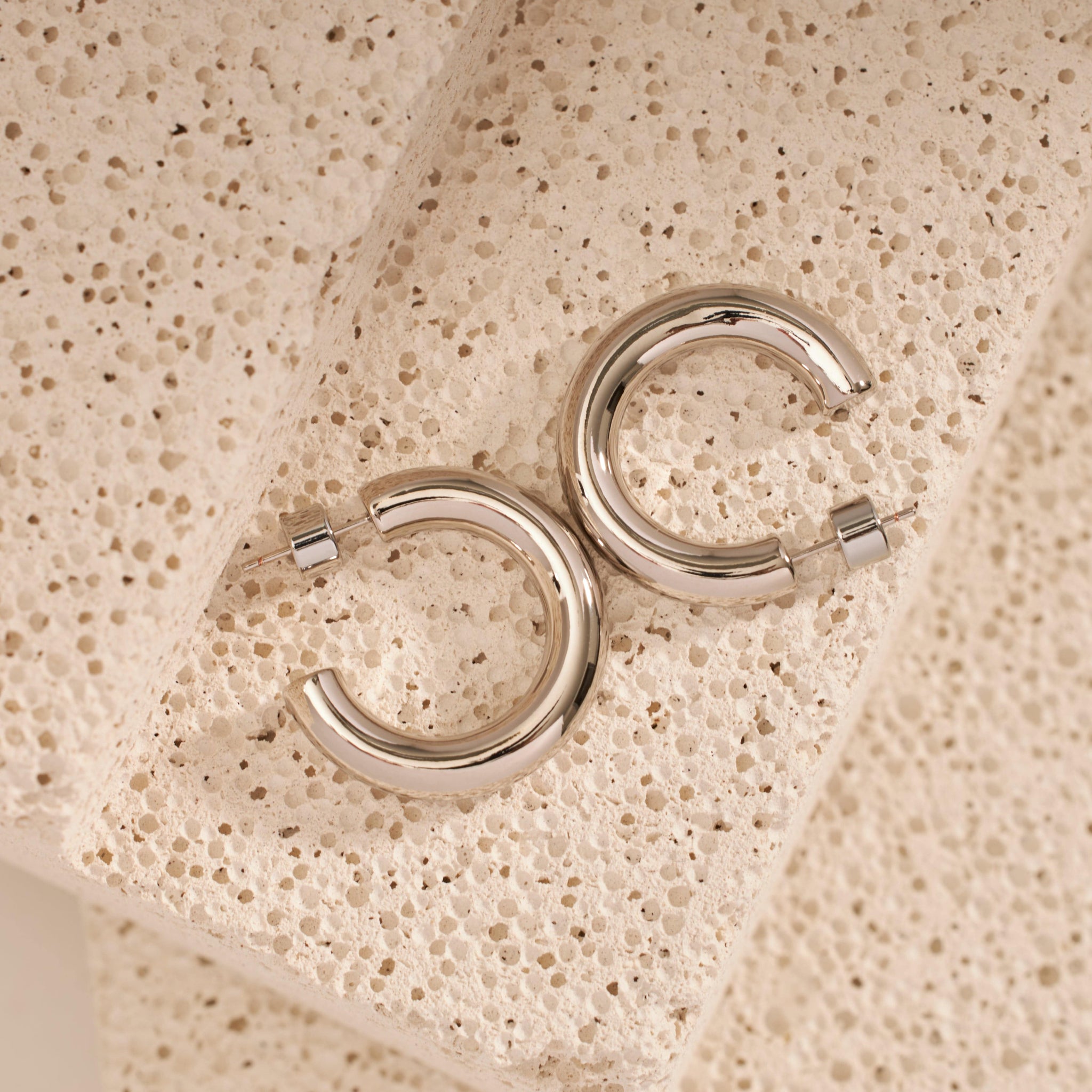 A pair of Perfect Hoop Midi Platinum earrings lays on a counter to show off the open hoop design and sleek finish.