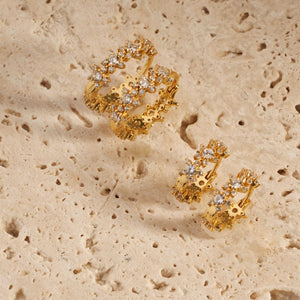 The Stella Hoop and Stella Hoop Mini earrings sit side-by-side on a stone surface, the star-shaped design clearly seen on the bottom part of the hoops as the crystal accents sparkle brightly on the upper sides. 