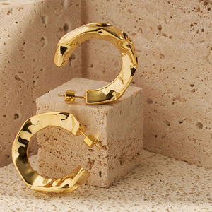 A pair of the Perfect Hoop Marquis earrings is displayed on a porous surface using a cube to offset the earrings. Each hoop is shown from a side view, displaying the open hoop design and hammered texture. 