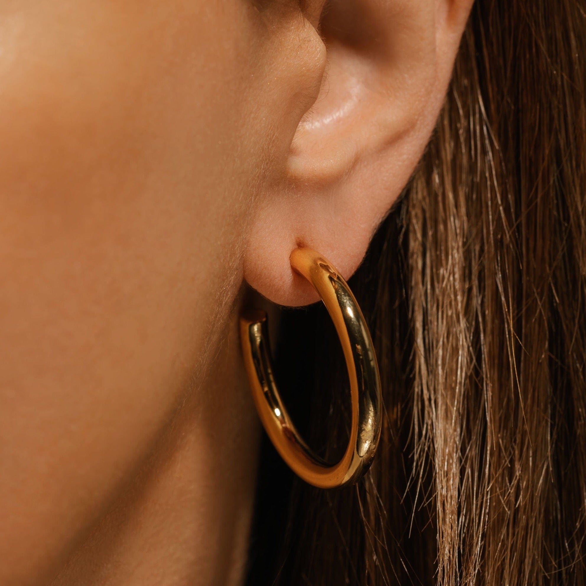 Model wearing The Malta Hoop 33 mm in gold, demonstrating its mid-size scale and comfortable push-back design.