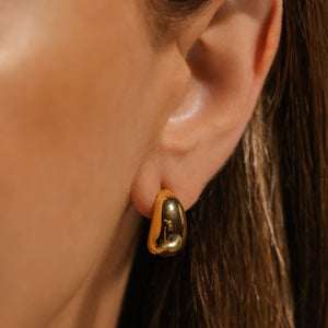 The model has her hair pulled behind her ear to show off the golden Amadora Hoop Mini adorning it. 