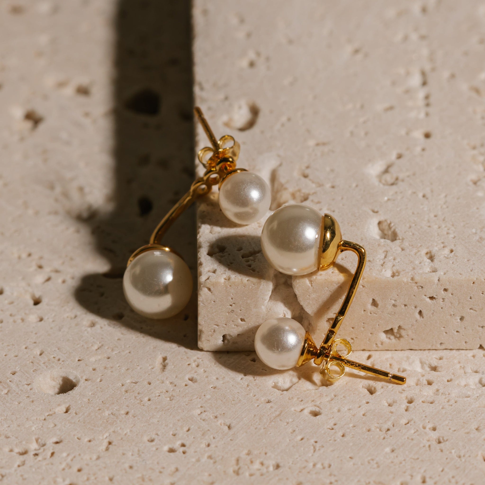 A pair of Perla Ear Jackets lays propped up on a stone countertop, the pearls glistening under the light.