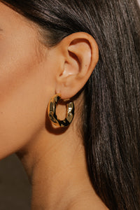 A close-up view shows the Perfect Hoop Marquis on the model's ear, the hammered texture creating reflections and shadows  on the surface of the hoop. 