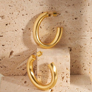 A pair of Ferrara Hoops reflect the light and shadows on their chunky surface.