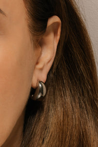 The broad, domed curve of an Amadora Hoop Platinum earring glistens as it adorns the model's ear.