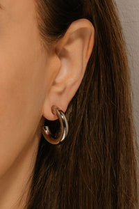 A close view shows the classy Perfect Hoop Midi Platinum earring adorning the model's ear. 